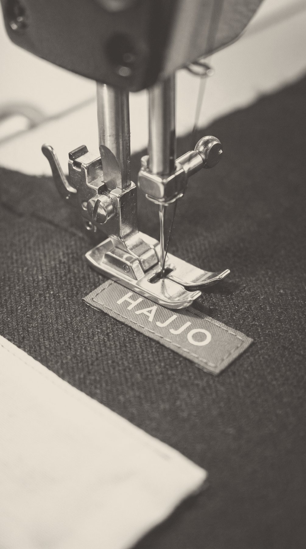 A woven brand label being stitched onto dark cloth under the presser foot.
